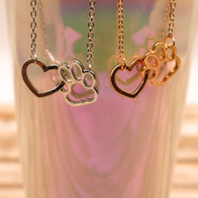 Load image into Gallery viewer, Gold tone and silver tone necklaces with open heart charms intertwined with open pet paw charms.  Displayed hanging from irridescent cup. 
