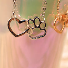 Load image into Gallery viewer, Gold tone and silver tone necklaces with open heart charms intertwined with open pet paw charms.  Displayed hanging from irridescent cup. 
