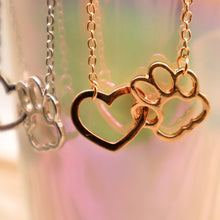 Load image into Gallery viewer, Gold tone and silver tone necklaces with open heart charms intertwined with open pet paw charms.  Displayed hanging from irridescent cup. 
