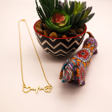 Load image into Gallery viewer, Gold tone necklace with open heart, heartbeat rhythm, and open pet paw.  Displayed beside succulent plant with a cute mosaic dachsund figurine. 
