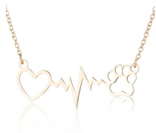 Load image into Gallery viewer, Gold tone necklace with open heart and paws connected by a heartbeat rhythm.  Diplayed on white background. 
