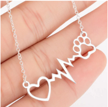 Load image into Gallery viewer, Silver necklace with open heart, heartbeat rhythm, and open pet paw.  Displayed on open hand.  
