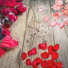 Load image into Gallery viewer, Silver tone necklace with open heart charms intertwined with open pet paw charms. Displayed on background with wood, roses, and flower petals.
