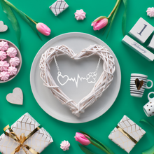 Load image into Gallery viewer, Silver tone necklace with open heart and paws connected by a heartbeat rhythm.  Diplayed on teal colored background with flowers, mugs, and a woven heart wreath. 
