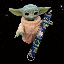 Load image into Gallery viewer, Picture of a Yoday doll with a silver round charm with the outline of Yoday and the words &quot;May the Force Be With You&quot; and a blue Charmable wristlet keychain with Grogu, the Mandalorian and the words &quot;Star Wars.&quot;   Displayed on a black night sky background. 
